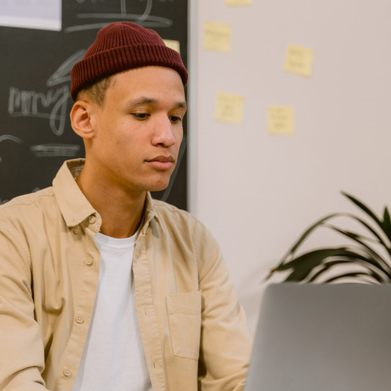 young man of color with beanie on working at laptop, ADHD assessment online, OAT